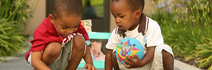 Photograph of two children looking at a book on the ground.